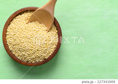 Yellow millet grain in wooden bowl with spoon on green background, Food ingredient, Top view 127341009