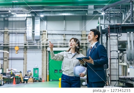 工場を視察する男性ビジネスパーソンと女性作業員 127341255
