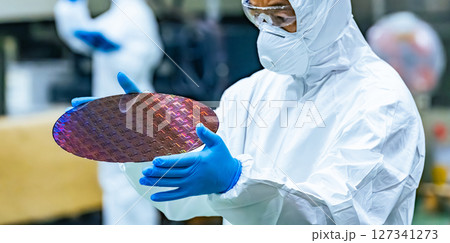 半導体工場でシリコンウエハーを検査する防塵服を着た男性作業員 127341273