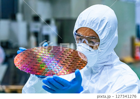 半導体工場でシリコンウエハーを検査する防護服を着た男性作業員 127341276