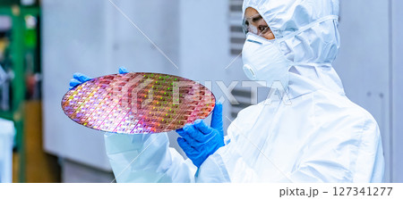半導体工場でシリコンウエハーを検査する防護服を着た女性作業員 127341277