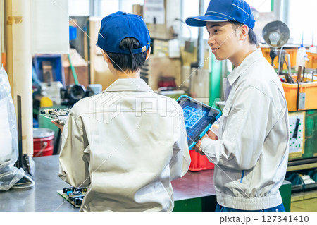 工場でタブレットを使って製品を検査する男女作業員 127341410