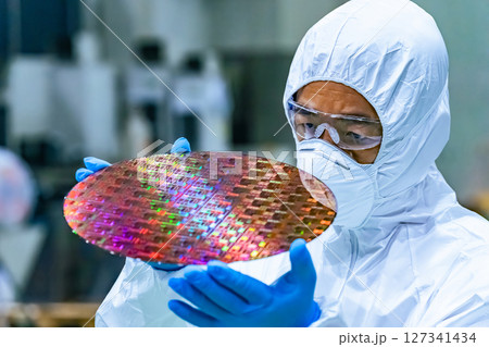 半導体工場でシリコンウエハーを検査する防護服を着た男性作業員 半導体工場でシリコンウエハーを検査する防護服を着た男性作業員 127341434