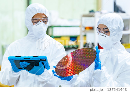 半導体工場でタブレットを持ってシリコンウエハーを検査する防護服を着た男女作業員 127341448