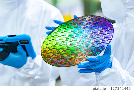 半導体工場でタブレットを持ってシリコンウエハーを検査する防護服を着た男女作業員 127341449