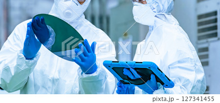半導体工場でシリコンウエハーを検査する防塵服を着た男性作業員 127341455