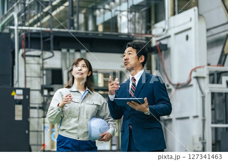 工場を視察する男性ビジネスパーソンと女性作業員 工場を視察する男性ビジネスパーソンと女性作業員 127341463