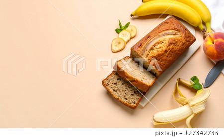 Banana Bread Delight: Slices of moist banana bread, adorned with banana slices and a peach, rest on a light beige surface, ready to be savored. A perfect image for food blogs and culinary websites. 127342735