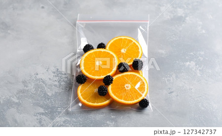 Fresh Fruit Sealed: A vibrant arrangement of juicy orange slices and plump blackberries, artfully enclosed within a transparent, sealed bag, ready for a delightful treat. 127342737