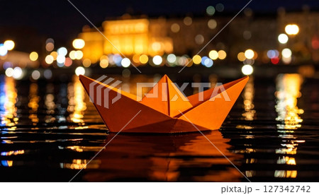 Nighttime Paper Boat: An orange paper boat floats serenely on dark water, reflecting city lights in the background. 127342742