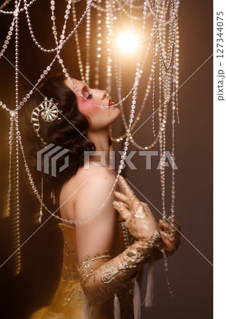 Retro-style performer in vintage costume posing on dark stage under chandelier 127344075
