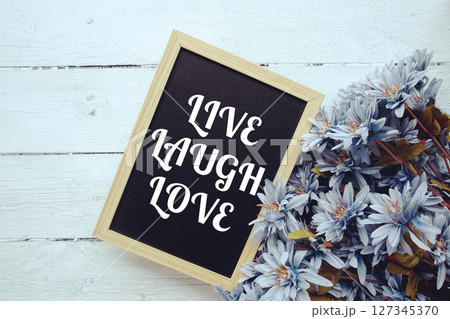 Live Laugh Love typography text written on wooden blackboard with flower bouquet decorate on wooden background 127345370