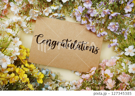 Congratulations text on paper card with flowers decoration on yellow background Congratulations text on paper card with flowers decoration on yellow background 127345385