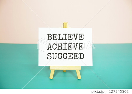 Believe Achieve Succeed text message on paper card with wooden easel Believe Achieve Succeed text message on paper card with wooden easel 127345502