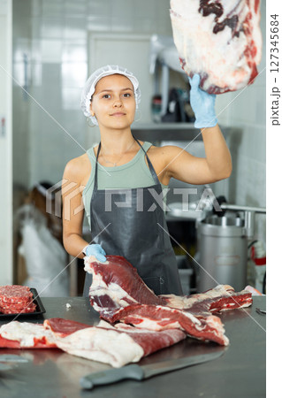Girl in butcher shop cuts meat carcass into small pieces of meat for retail sale in small store 127345684