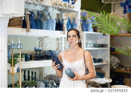 Woman examining decorative blue glass items in home decor store 127345835