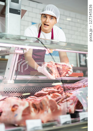 Positive young salesman demonstrating piece of meat in butcher shop 127345836