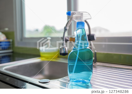 Blue cleaning spray bottle placed on silver kitchen sink with a faucet in background. Represents modern cleaning tools and hygiene in kitchen setting. Glass spray bottle emphasizes cleaning concept Blue cleaning spray bottle placed on silver kitchen sink with a faucet in background. Represents modern cleaning tools and hygiene in kitchen setting. Glass spray bottle emphasizes cleaning concept 127348286