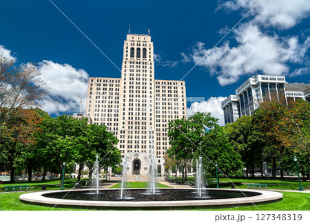 In Albany, United States, the art deco State Office Building towers behind park lawns and splashing fountains under a bright blue sky 127348319