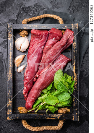 Mutton tenderloin fillet meat, raw lamb in wooden tray with herbs. black background. top view 127349568