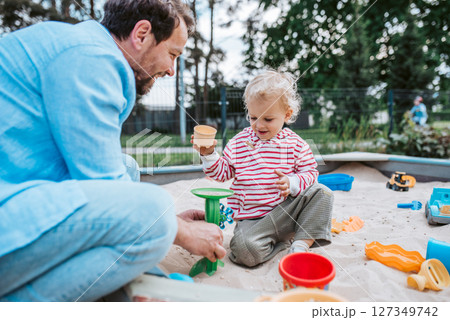 Father and little toddler son playing in the sandbox on playground. 127349742