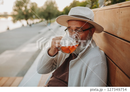 Senior man enjoying beer on sunny riverside promenade 127349754