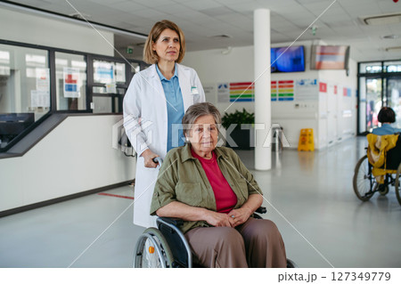 Geriatric doctor pushing a patient in a wheelchair down a hospital hallway. 127349779