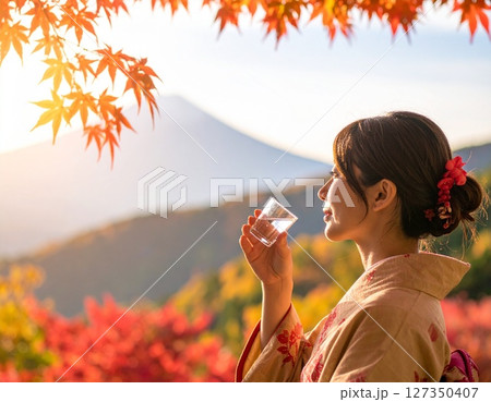 紅葉の山々を背景にひやおろしの日本酒を嗜む着物の日本人女性 127350407