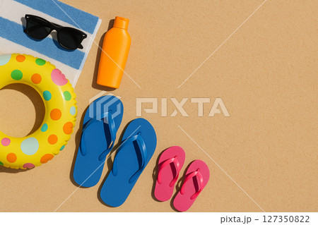 Colorful beach accessories including flip-flops, towel, sunglasses, sunscreen and inflatable ring on sand 127350822