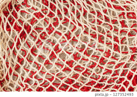 Red and beige rope mesh forming abstract pattern over rustic background. Handmade net design creates textured craft surface. Zero waste and plastic-free concept 127352493