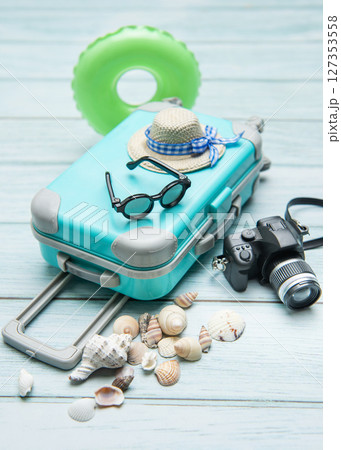 Turquoise suitcase, sunglasses, straw hat, inflatable ring, camera and seashells  127353558