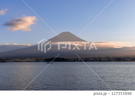 Serene view of Mount Fuji at sunset, partially veiled by clouds, with Lake Kawaguchi waters 127353898