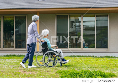 住宅の前を歩く車椅子に乗ったシニア夫婦 127353977