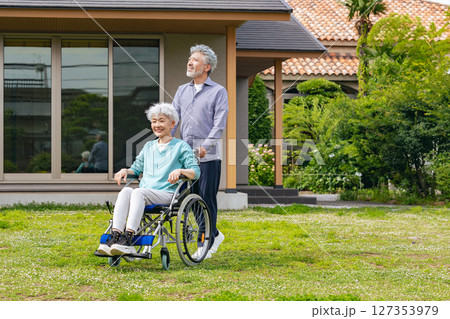 住宅の前を歩く車椅子に乗ったシニア夫婦 127353979