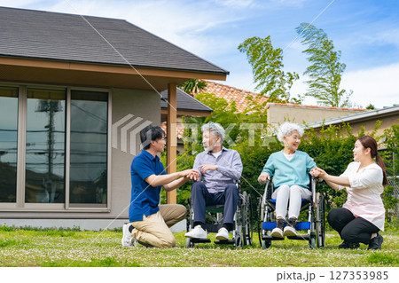 庭で会話する車椅子に乗ったシニア夫婦とケアスタッフ 127353985