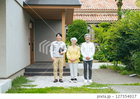 住宅の前で笑う男性作業員とシニアカップル 住宅の前で笑う男性作業員とシニアカップル 127354017