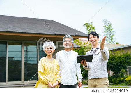 住宅の前で説明する男性作業員とシニアカップル 127354019