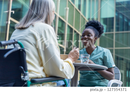 Nurse and female patient having lunch in the clinic yard and looking involved 127354371