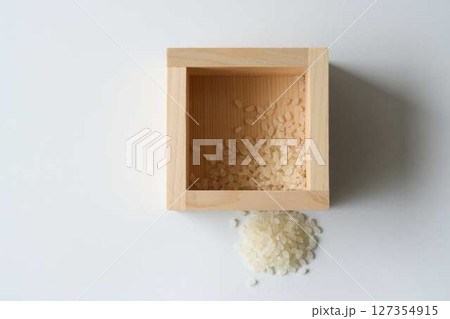 白背景に少しのコメが入った升とこぼれたコメ 127354915
