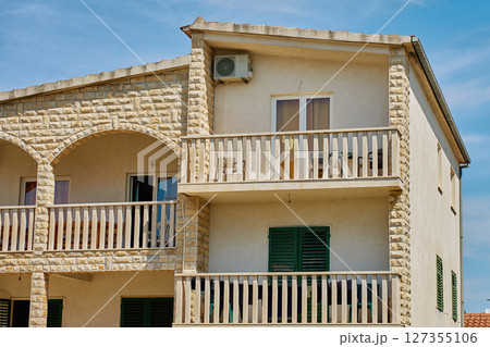 Stone facade house with balconies and shutters under blue sky Stone facade house with balconies and shutters under blue sky 127355106