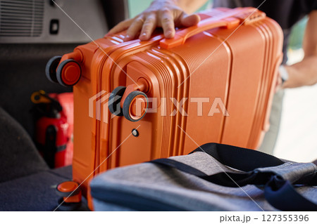 Close-up of loading orange suitcase in car trunk, inside view Close-up of loading orange suitcase in car trunk, inside view 127355396