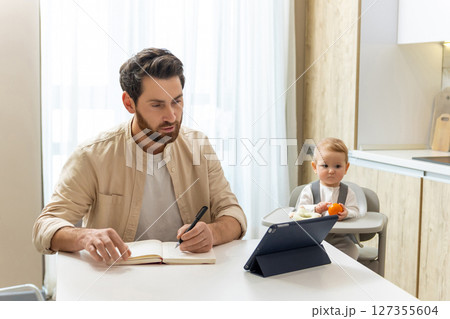 Young father working from home, his baby boy playing next to him Young father working from home, his baby boy playing next to him 127355604
