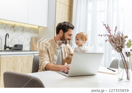 Bearded young caucasian man working from home while taking care of his little son 127355659