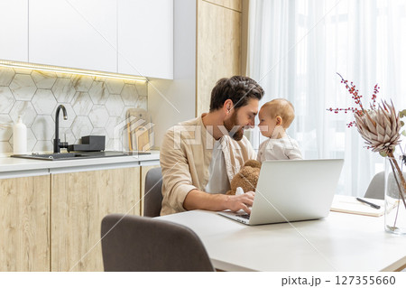 Bearded young caucasian man working from home while taking care of his little son Bearded young caucasian man working from home while taking care of his little son 127355660