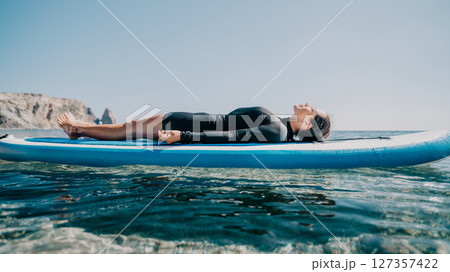 Woman sup yoga. Happy sporty woman practising yoga pilates on paddle sup surfboard. Female stretching doing workout on sea water. Modern individual female hipster outdoor summer sport activity. Woman sup yoga. Happy sporty woman practising yoga pilates on paddle sup surfboard. Female stretching doing workout on sea water. Modern individual female hipster outdoor summer sport activity. 127357422