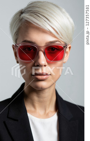 White woman with short pixie cut and red-tinted rectangular glasses, her confident eyes framed by sharp angular patterns, representing transformation White woman with short pixie cut and red-tinted rectangular glasses, her confident eyes framed by sharp angular patterns, representing transformation 127357581