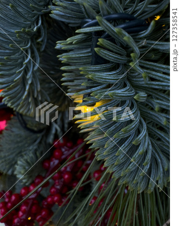 Close-up of illuminated artificial pine branches and red berries creating a festive christmas atmosphere 127358541