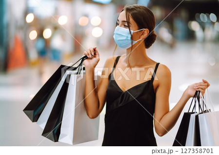 Fashionable woman in protective medical mask with shopping bags walking in the mall. Covid-19. 127358701