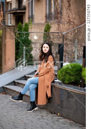 Serene afternoon in an urban park with a young woman enjoying nature while sitting on stone steps surrounded by greenery and modern architecture in soft golden light 127358743