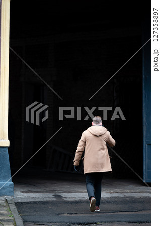 A man dressed in a brown coat is making his way through a shadowy doorway on a brisk afternoon in an abandoned cityscape. The air is chilly, and the atmosphere is eerily quiet 127358897